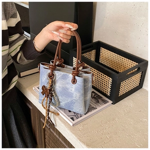 Detail of light blue denim tote bag featuring brown woven handle and pearl charm accents