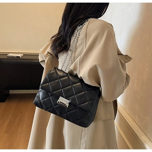 Detail shot of black quilted shoulder bag with silver chain strap and metal lock buckle