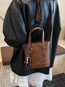 Brown leather bucket bag with top handles and ethnic bead charm worn by a model