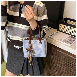 Detail showing blue cloud-textured bucket bag with leather handle and tassel charm decor