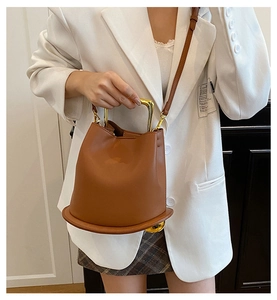 Detail of a brown leather bucket bag with gold U-shaped handle and leather shoulder strap
