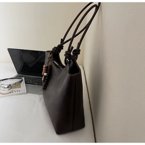Detail of dark brown tote bag featuring textured faux leather and wooden bead tassel