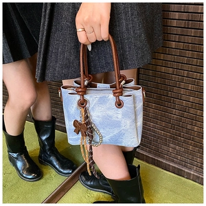 Detailed macro view of denim blue bucket bag featuring dark brown rope handles and bow charm