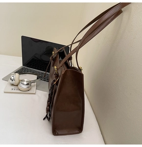 Detail view of a vintage brown leather tote bag with a striped charm and golden buckle