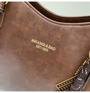 Close-up of brown vintage leather tote with gold logo and abacus pendant detail