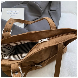 Detail of brown suede tote bag featuring striped lining and silver zipper closure
