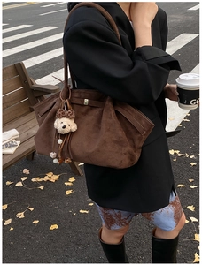 Detail der braunen Wildleder-Hobo-Tasche mit Bärenanhänger in herbstlicher Straße