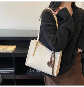 Detail of off-white tote bag with gold logo and brown tassel charm on adjustable strap