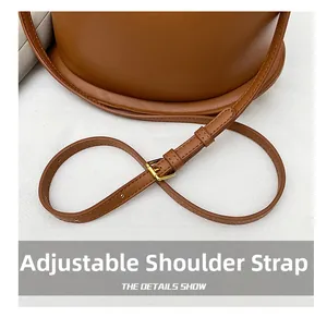 Detailed close-up of the adjustable leather shoulder strap with golden buckle on a brown bag