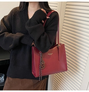 Close-up of burgundy leather tote bag with logo detail and braided charm on a model