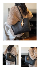 Detail of black leather tote bag featuring a decorative wooden beaded tassel charm