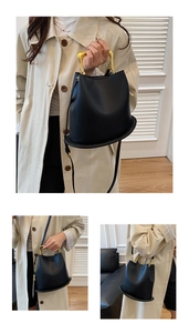 Detail of black leather bucket bag with distinctive gold U-shaped metal handle and strap