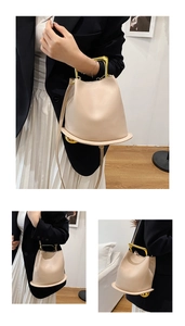 Detailed view of beige bucket bag featuring U-shaped gold metal handles and wide circular base
