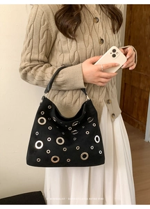 Minimalist black tote bag with silver eyelet details worn over the shoulder with a beige knit sweater