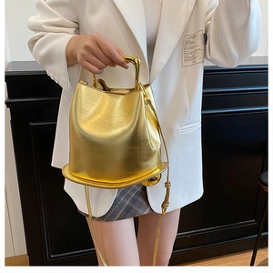 Detail of a metallic gold bucket bag with a flat wide base and U-shaped metal handles
