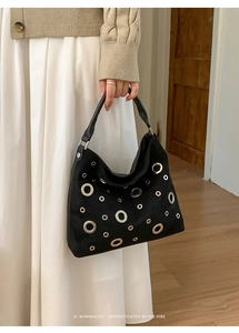 Detail of black suede hobo bag with silver metallic eyelets held by a model in casual outfit