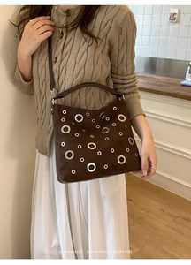 Brown suede shoulder bag with gold and silver metal eyelets shown in a lifestyle setting