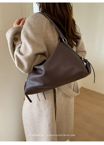 Detail of a minimalist dark brown hobo shoulder bag in soft leather on a model's shoulder