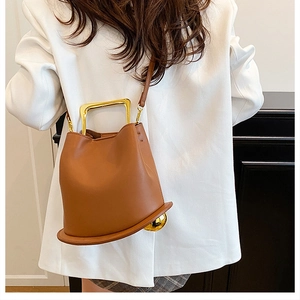 Detailed view of brown leather bucket bag featuring gold U-shaped handle and side metal spheres