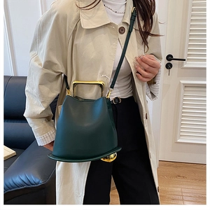 Deep green leather bucket bag with unique gold U-shaped handle and metal ball detail