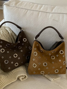 Chic suede tote bags with silver eyelets in brown and tan tones on a sofa
