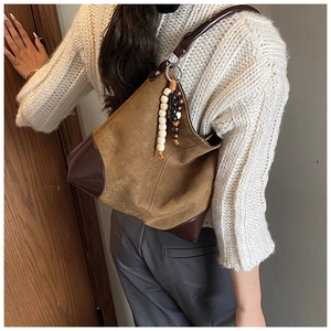 Detail of brown suede hobo bag featuring dark patent leather trim and beaded pendant
