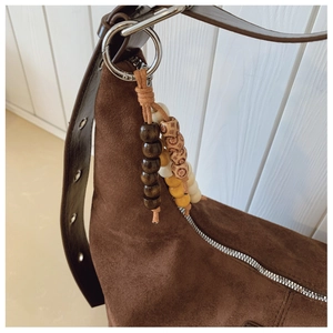 Detail of coffee brown suede tote bag featuring ethnic wood bead charm and metal hardware