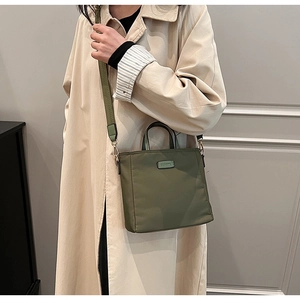 Olive green nylon tote bag with wide adjustable shoulder strap worn by a female model
