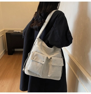 Detail of canvas shoulder bag showing front flap pockets and utilitarian metal buckles