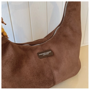 Close-up of brown suede crescent bag with leather logo tag and decorative wooden beads