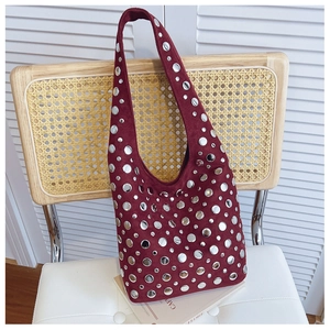 Detail of burgundy suede bucket bag featuring silver punk rivets on a woven chair