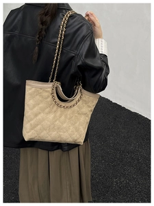 Close-up of beige quilted tote bag with chain strap and dual handles worn by model