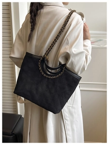 Detail of black quilted suede tote bag with chain strap worn with a beige trench coat