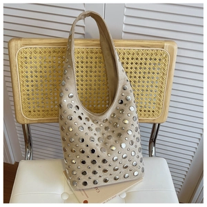 Detail of beige suede shoulder bag with silver rivet studs on a rustic rattan chair