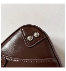 Close-up of premium dark burgundy leather texture with silver rivets on a saddle bag