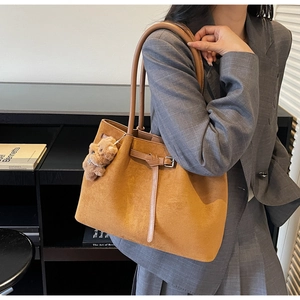 Detail of caramel suede tote bag featuring a plush bear pendant on a grey blazer model