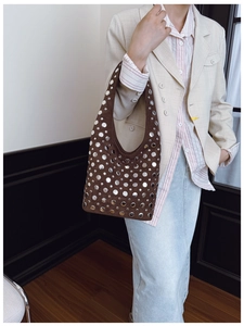 Close-up of dark brown suede bucket bag with silver metal rivets on a model wearing a blazer