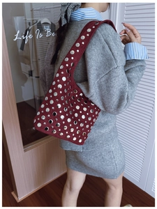 Detail of burgundy suede tote bag featuring silver rivet accents and shoulder strap style