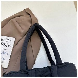 Detail of black quilted puffer tote bag with thick padded handles and nylon finish
