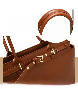 Detail of brown leather handbag featuring gold metal buckle and textured handle stitching