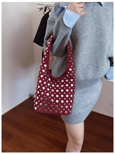 Detail of burgundy suede bucket bag with various sized silver metallic studs on strap