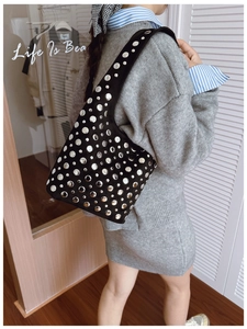 Detail of black suede hobo bag with silver metallic rivets worn by a model
