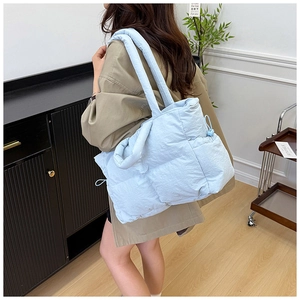 Light blue quilted nylon tote bag worn by a model in a cozy indoor setting