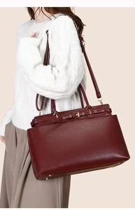 Detail of burgundy tote bag with gold hardware and removable shoulder strap worn by model