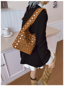 Brown suede hobo bag with silver studs worn by a model in a minimalist room