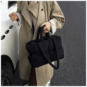 Close-up of black quilted puffer tote bag with handles and crossbody strap in street setting