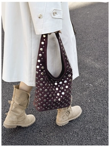 Street style shot of a burgundy suede bucket bag with decorative silver metal rivets