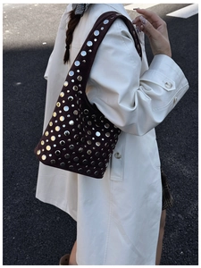 Close-up of dark suede bucket bag featuring silver metal rivets and punk style design