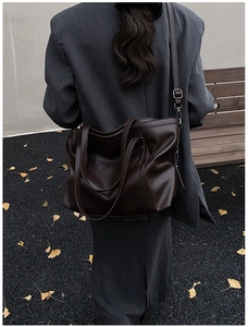 Sac fourre-tout en cuir marron foncé porté en bandoulière sur un blazer gris en décor d'automne