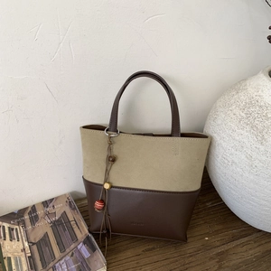 Detail view of dual-material tote bag with artistic tassel charm on a wooden surface